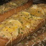 A close-up of freshly baked cheesy garlic bread with melted cheese and golden crust.